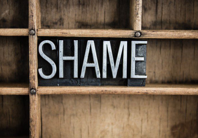 Standing on a wooden shelf are letters spelling out the word shame balanced. Each letter is carved out to create a stamp.